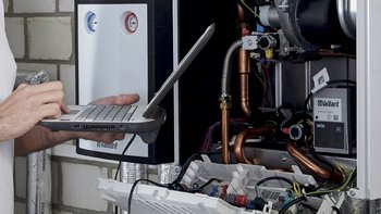 Der Handwerker überprüft die Heizungsanlage, während er auf seinem Laptop Informationen eingibt oder abruft.